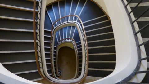 Bild eines Treppenhauses im OLG Köln, von oben nach unten fotografiert, sodass sich das Bild einer Abwärtsspirale ergibt,